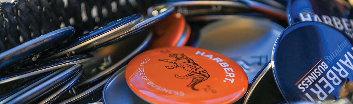 A wide, shallow-depth-of-field close-up shot of a pile of various promotional Auburn Harbert College of Business pin-back buttons