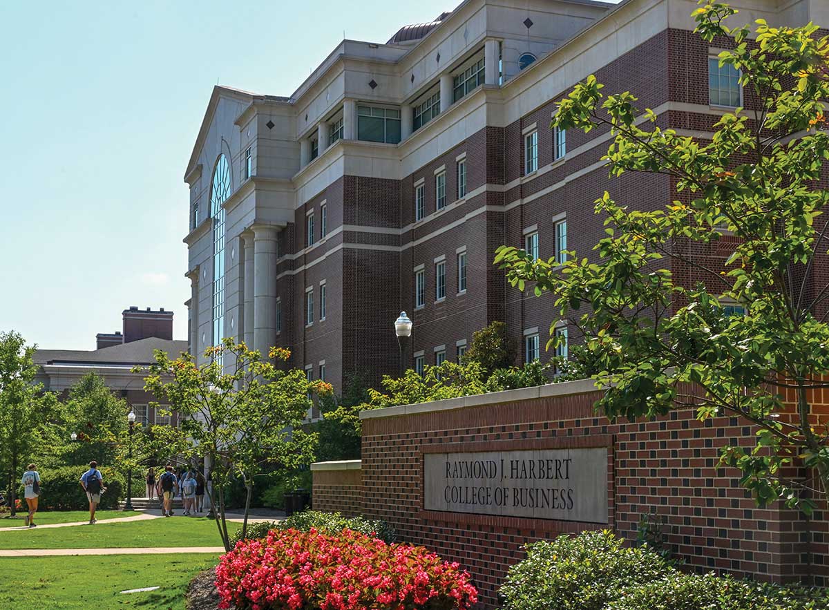 Outdoor shot of the Raymond J. Harbert College of Business building on a sunny day showing college students walking nearby on a path