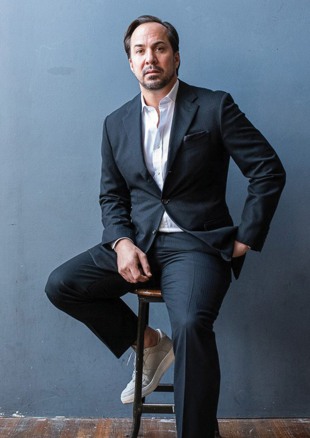 Patrick Klesius in business suit attire seated on a round stool chair
