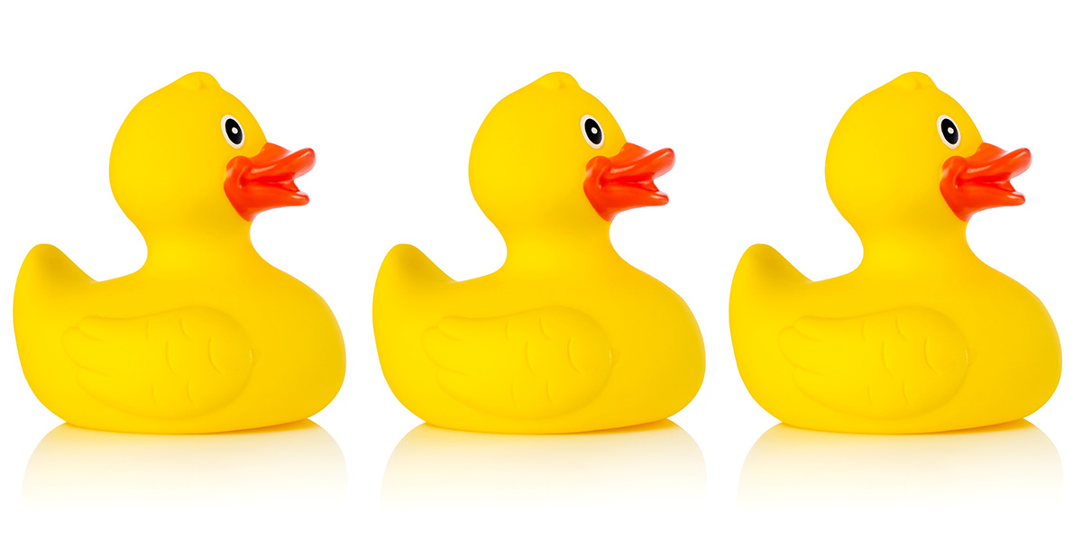 Three identical yellow rubber ducks sitting in a row against a white background.